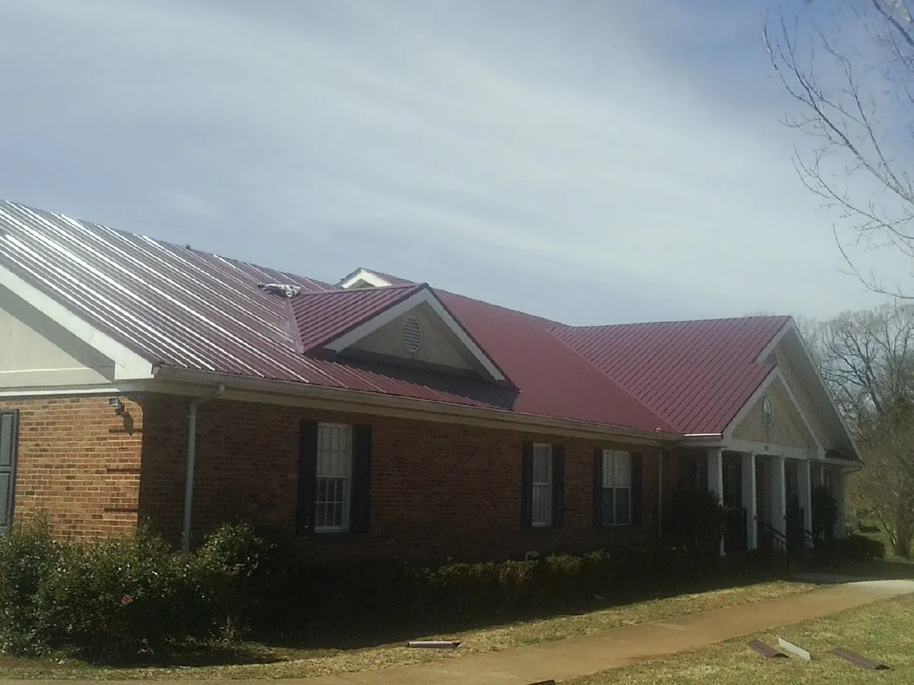Red metal roof with gabled entries on a long brick building, from a Hail Damage Roof Repair job in Wenonah