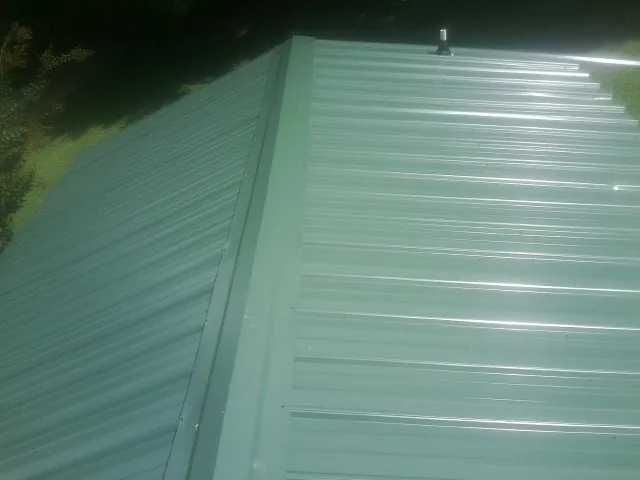New green metal panels meeting at the ridge of a roof — Flat Roof Repair work by our crew in Wenonah