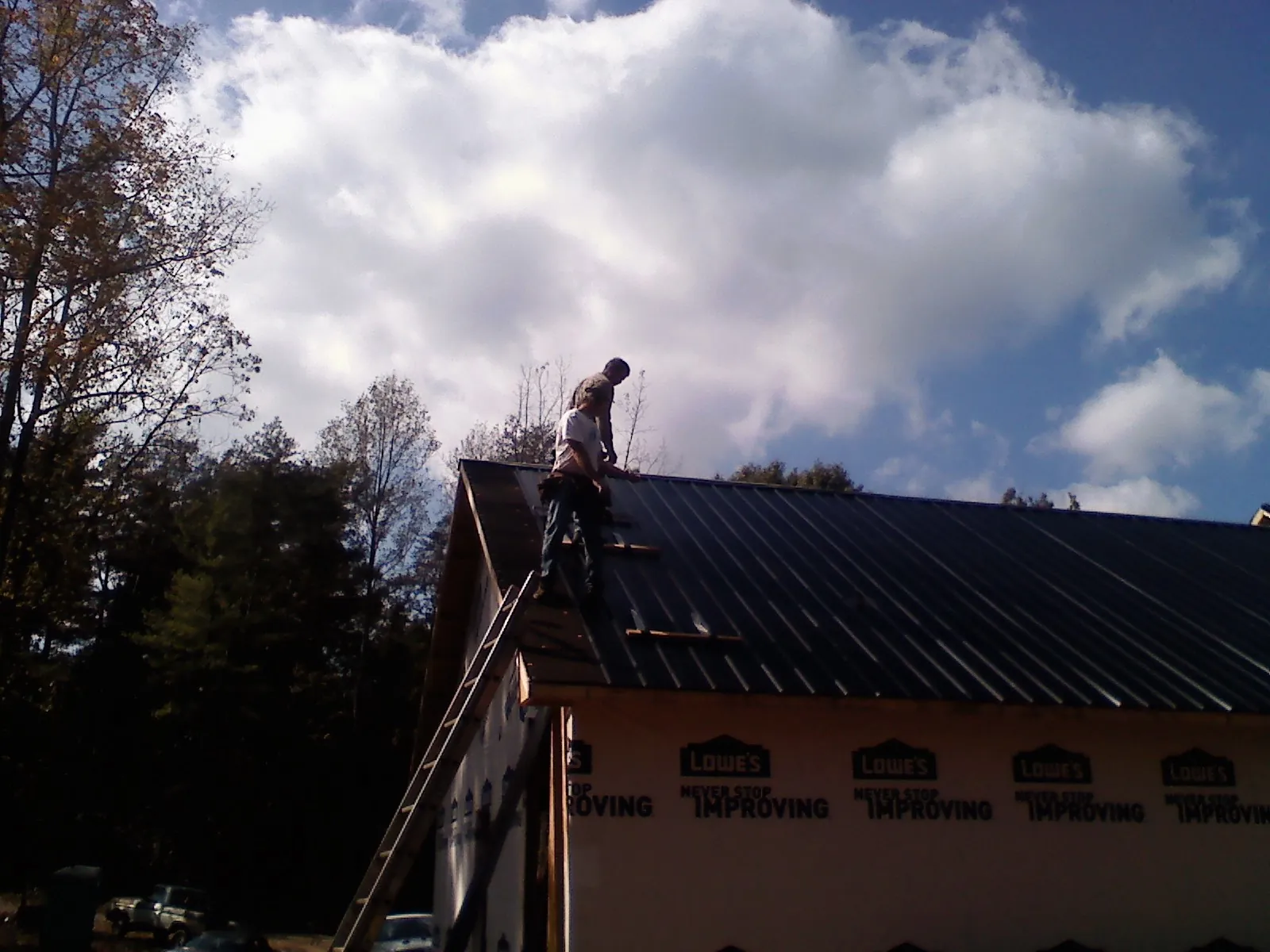Roofer fastening dark metal panels high against a cloudy sky, from a Roof Inspection job in Wenonah