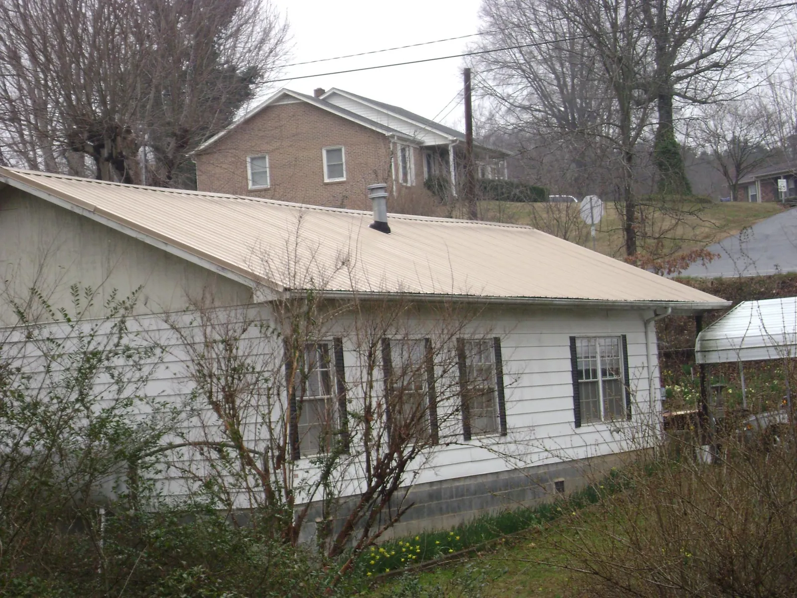 Tan metal roof on a white sided house set into a hillside — Commercial Roofing by Roofing Brothers in Wenonah